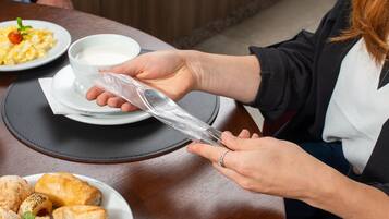 Una persona sosteniendo una bolsa de plástico transparente sobre una taza blanca, sobre una mesa con un plato de pasteles y un tazón de sopa.