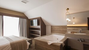 A modern hotel bathroom with a bathtub, a vanity with a mirror, and a television mounted on the wall. - Hotel Fioreze Primo (Gramado)