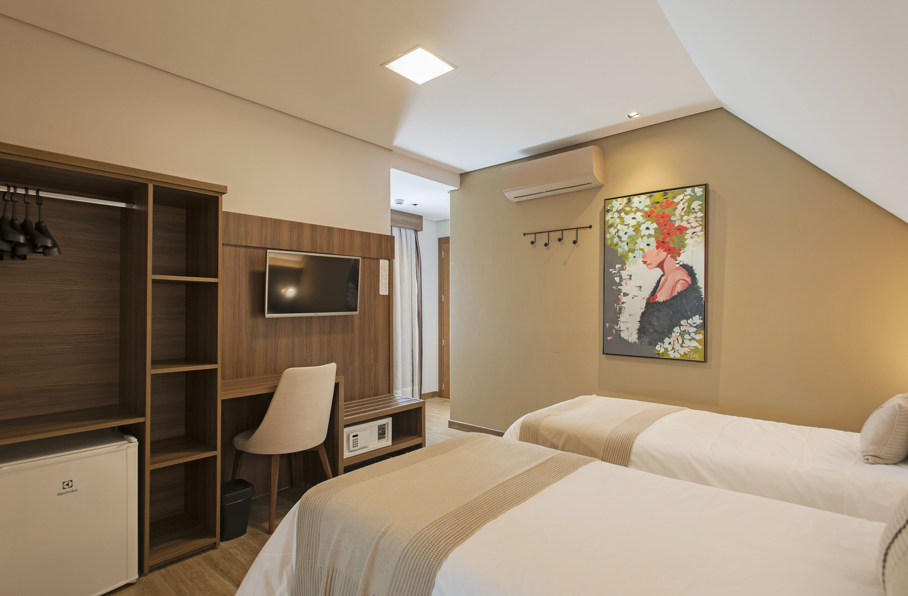 A hotel room with two beds, a TV, a wardrobe, and a painting on the wall.