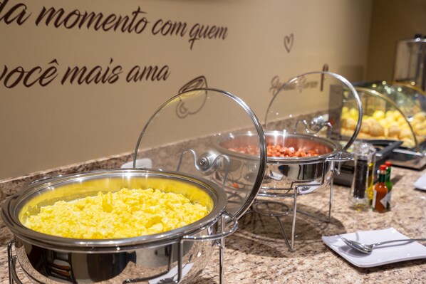 Montaje de bufé con diversos alimentos en recipientes transparentes, una pared con diseño de corazón y condimentos en la barra.