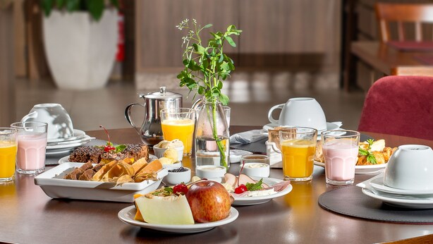 A breakfast table with various dishes, drinks, and a vase of flowers. - Hotel Fioreze Primo (Gramado)