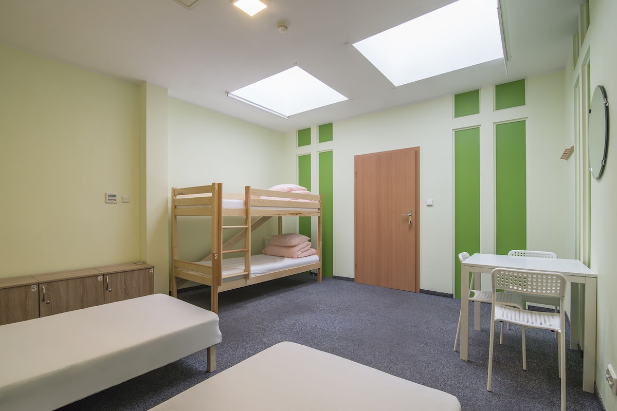Quarto em dormitório com beliches, uma escrivaninha e uma cadeira.