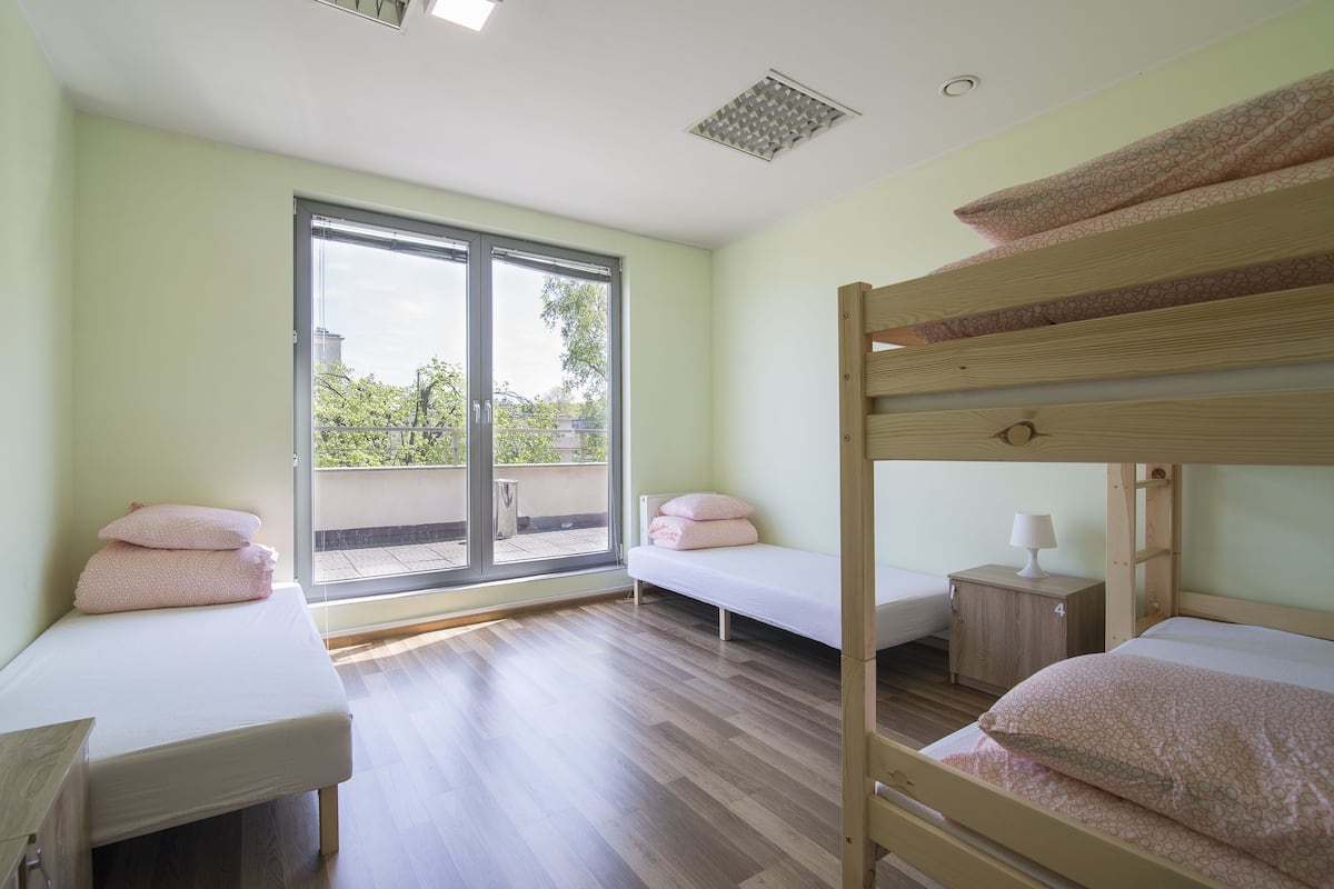 Quarto com duas camas de solteiro, uma pequena mesa de cabeceira de madeira e uma janela ampla com vista para o exterior.