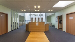 Un espace d’accueil doté d’un comptoir de réception en bois, d’une enseigne indiquant la réception et offrant une vue sur la ville grâce à de grandes fenêtres.