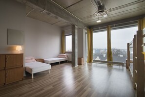 A modern, minimalist room with a wooden floor, a bed, a bench, and a window with curtains. - Sea Hostel (Gdynia)