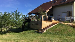 A house with a wooden staircase leading to a deck, surrounded by greenery. - 220 m² house, sleeps 8–10. With private grounds and a terrace overlooking the lake and spa (Hautecour)