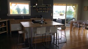 A modern kitchen with a central island, white chairs, and a dining table with clear chairs. - 220 m² house, sleeps 8–10. With private grounds and a terrace overlooking the lake and spa (Hautecour)