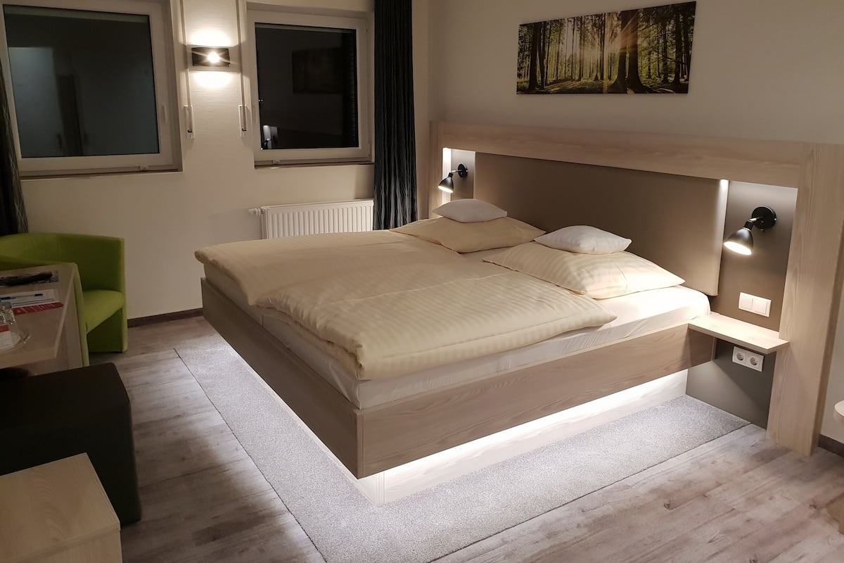 A modern bedroom with a large bed, bedside lamps, a window, and a painting on the wall.