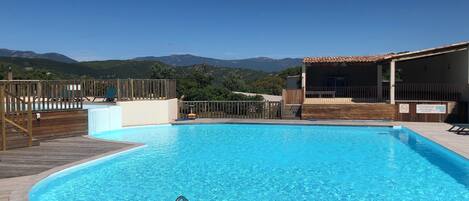 A swimming pool with a wooden deck, a lifeguard chair, and a view of mountains in the background.