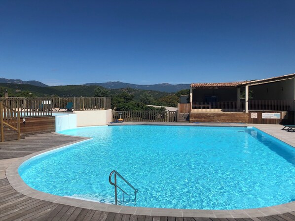 A swimming pool with a wooden deck, a lifeguard chair, and a view of mountains in the background.