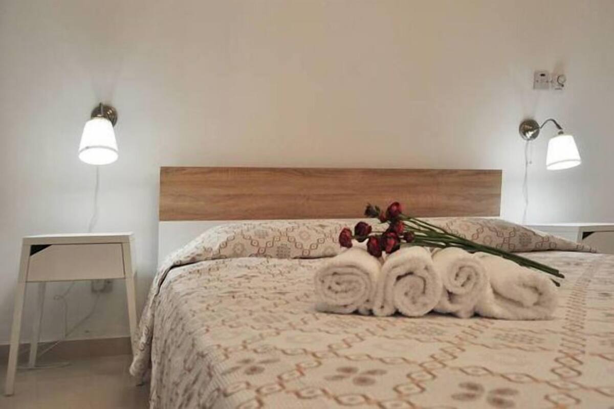 Una cama bien hecha con toallas dobladas y un ramo de flores, un cabecero de madera y lámparas de noche.
