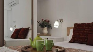 A neatly arranged bedroom with a bed, bedside table, lamp, and a tray with green cups and a teapot. - Royal Sunset Studios (Limassol)