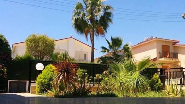 A residential building with a white facade, a balcony, and lush greenery including palm trees and various shrubs. - Royal Sunset Studios (Limassol)