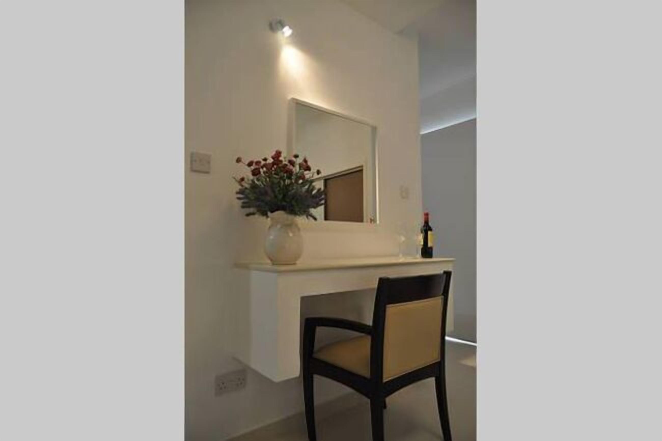 A modern room with a white console table, a vase with red flowers, a mirror, and a chair.