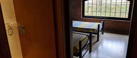 Una habitación con dos camas, un ventanal con vistas a un área verde y una pared de azulejos.