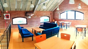 A spacious indoor area with brick walls, multiple tables and chairs, and a large screen displaying a graph. - Alberg Rural Ruta del Ferro (Sant Joan de Les Abadesses)