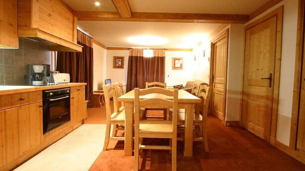 Una cocina de madera con una mesa de comedor y sillas, un horno empotrado y una cafetera.