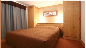 Un dormitorio con una cama grande, paneles de madera, un cuadro enmarcado en la pared y una cortina.