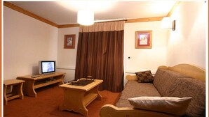 Una sala de estar acogedora con un mueble bajo de madera para el televisor, una mesita, un sofá con cojines y una cortina.