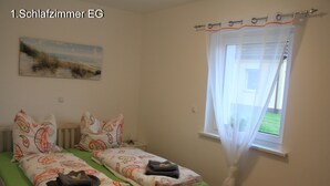 A bedroom with two beds, each with patterned bedding and pillows, a painting on the wall, and a window with a curtain.