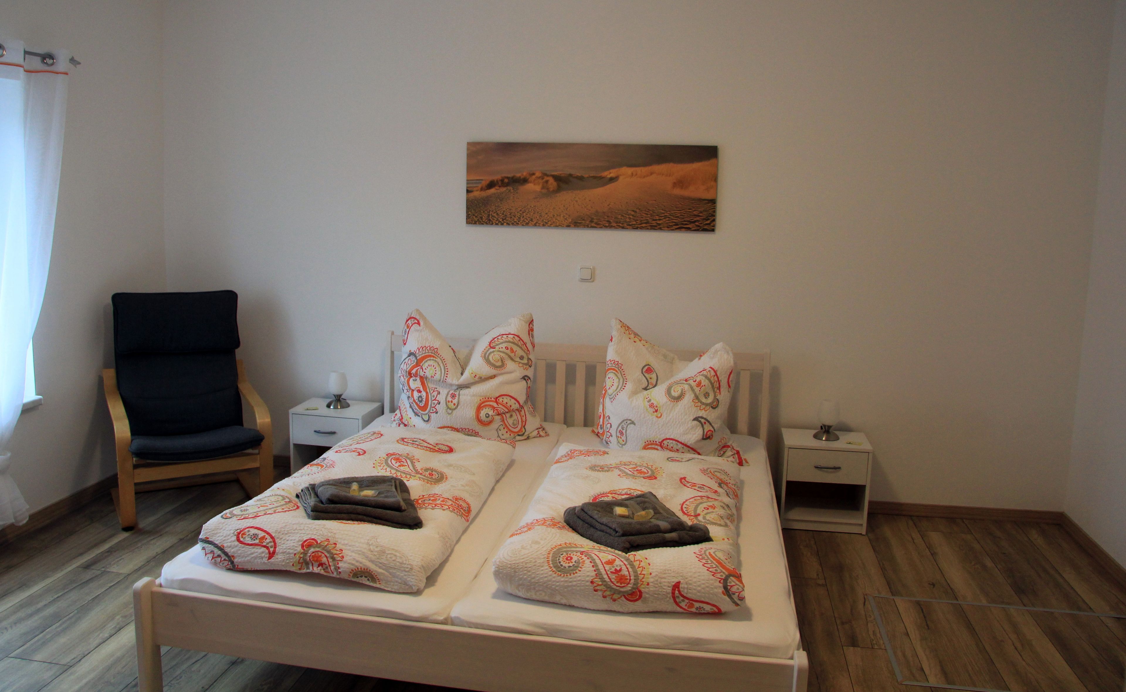 Ein Schlafzimmer mit einem Bett, zwei Nachttischen, einem Sessel und einem Bild an der Wand.