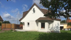 A single-story house with a white exterior and a brown roof, surrounded by a well-maintained lawn.