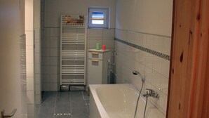 A modern bathroom with a large bathtub, a shower, and a toilet. There is a towel rack and a small shelf with toiletries.