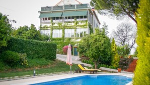 A swimming pool with two sun loungers, a pink umbrella, and a building with ivy-covered walls in the background. - Vila dos Castanheiros (Ferreira do Zezere)