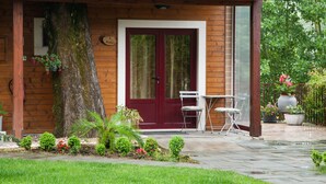 A wooden cabin with a tiled roof, a red door, and a small patio with a table and chairs. - Vila dos Castanheiros (Ferreira do Zezere)