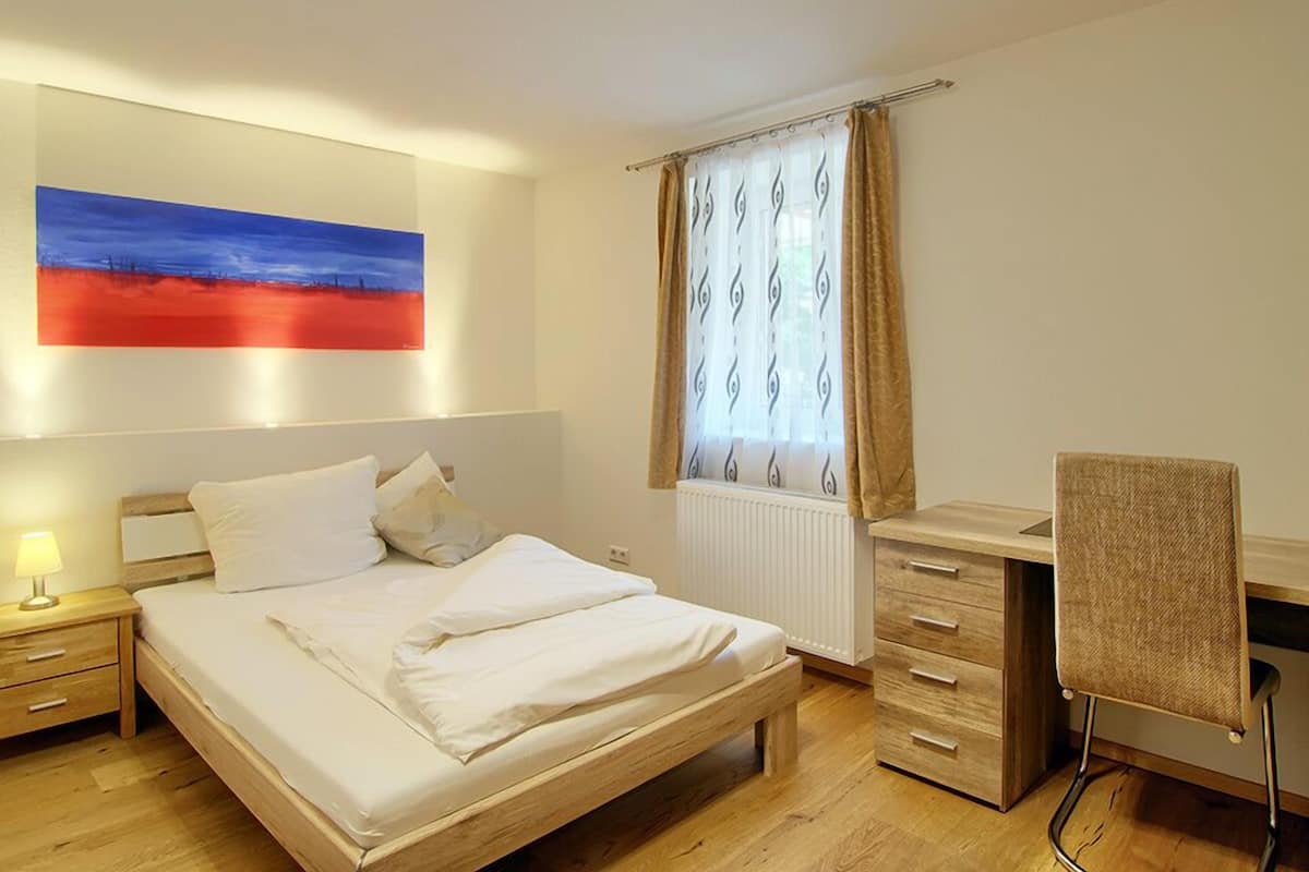 Une chambre à coucher comprenant un lit, une table de chevet, une lampe et un bureau avec une chaise.