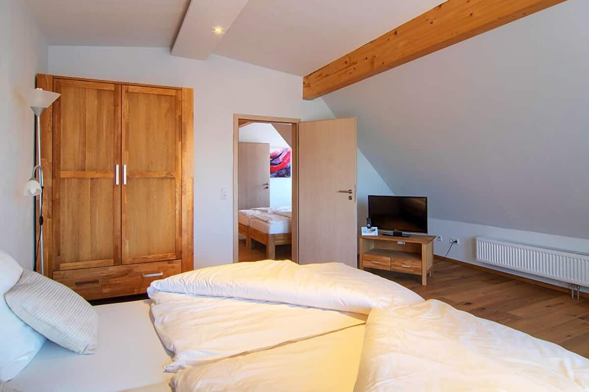 Une chambre avec une grande armoire, un lit avec une literie blanche, un téléviseur posé sur un meuble en bois et un radiateur fixé au mur.