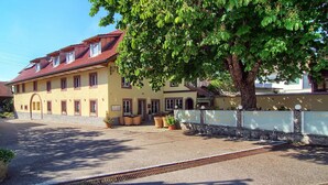 A yellow building with a red roof, a paved entrance, and a tree in front.