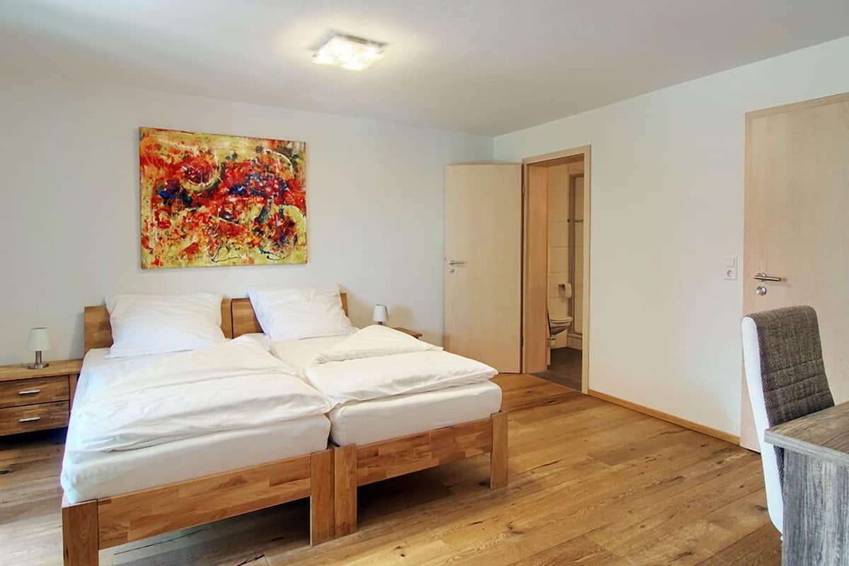 Un lit double avec un cadre en bois, une table de chevet, une lampe et un tableau abstrait aux couleurs vives accroché au mur.