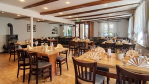 A restaurant with wooden tables and chairs, a fireplace, and large windows.