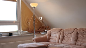 Una sala de estar moderna con un sofá color beige, una mesa de centro de vidrio, una lámpara de pie y un ventanal con persianas.