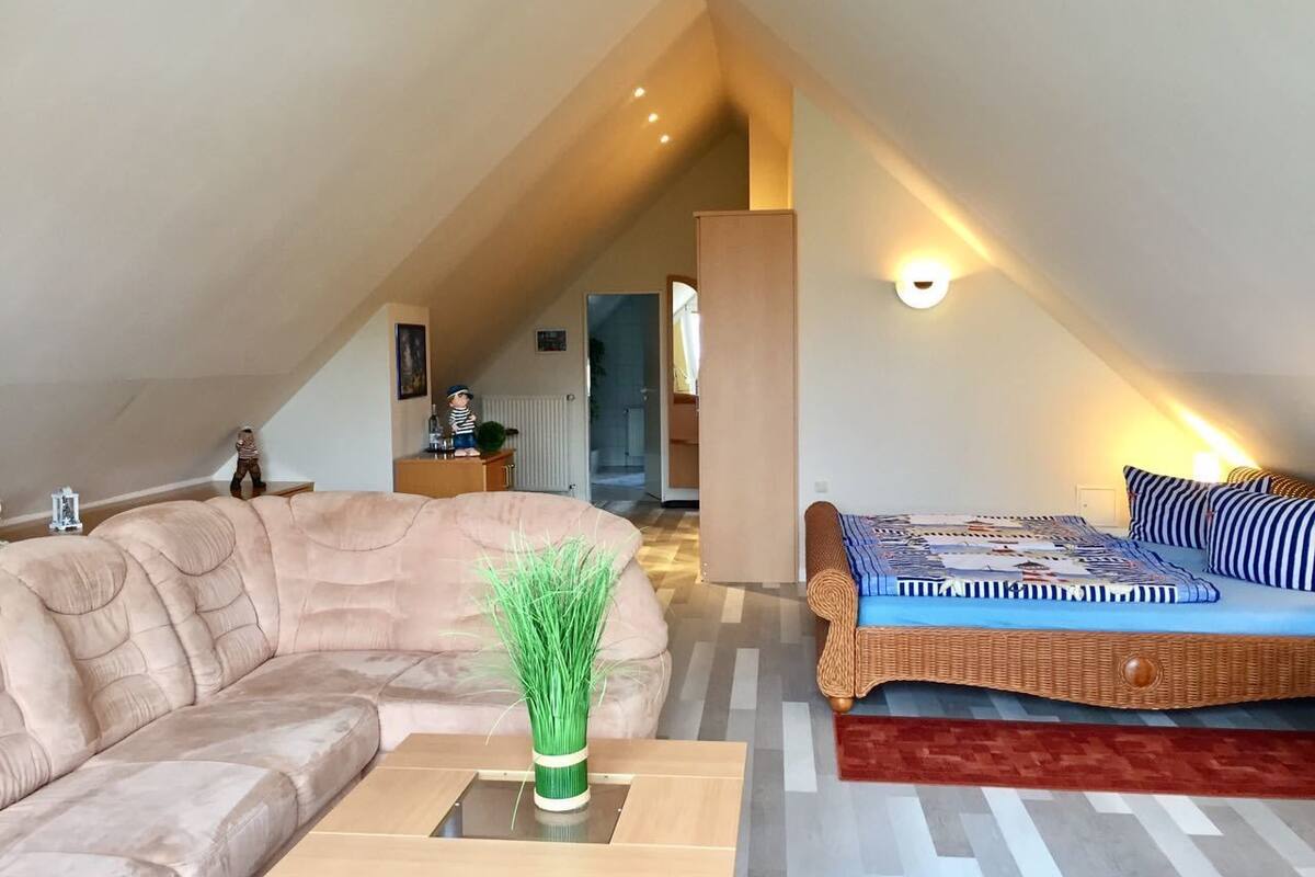 A cozy loft bedroom with a large bed, a sofa, and a small table with a vase.