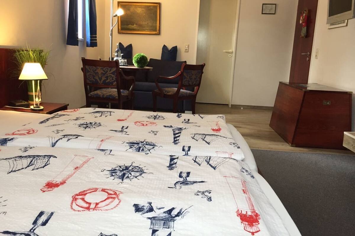 A hotel room with a bed, a desk, a chair, a lamp, and a door.