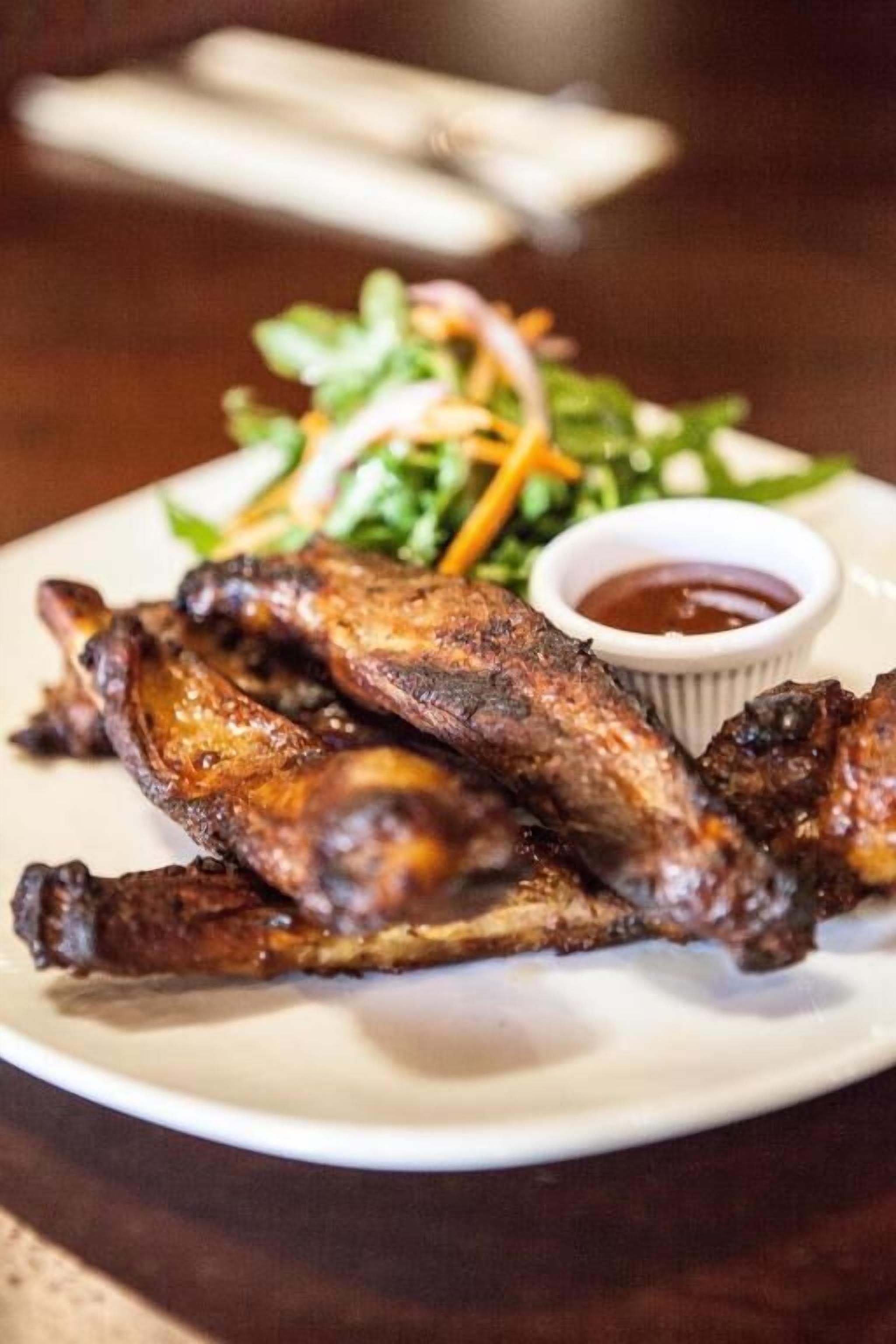A plate of grilled chicken wings with a side salad and dipping sauce.