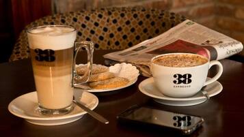 A table with a coffee cup labeled "38 ESPRESSO," a tall glass of coffee, a plate with cookies, and a newspaper.