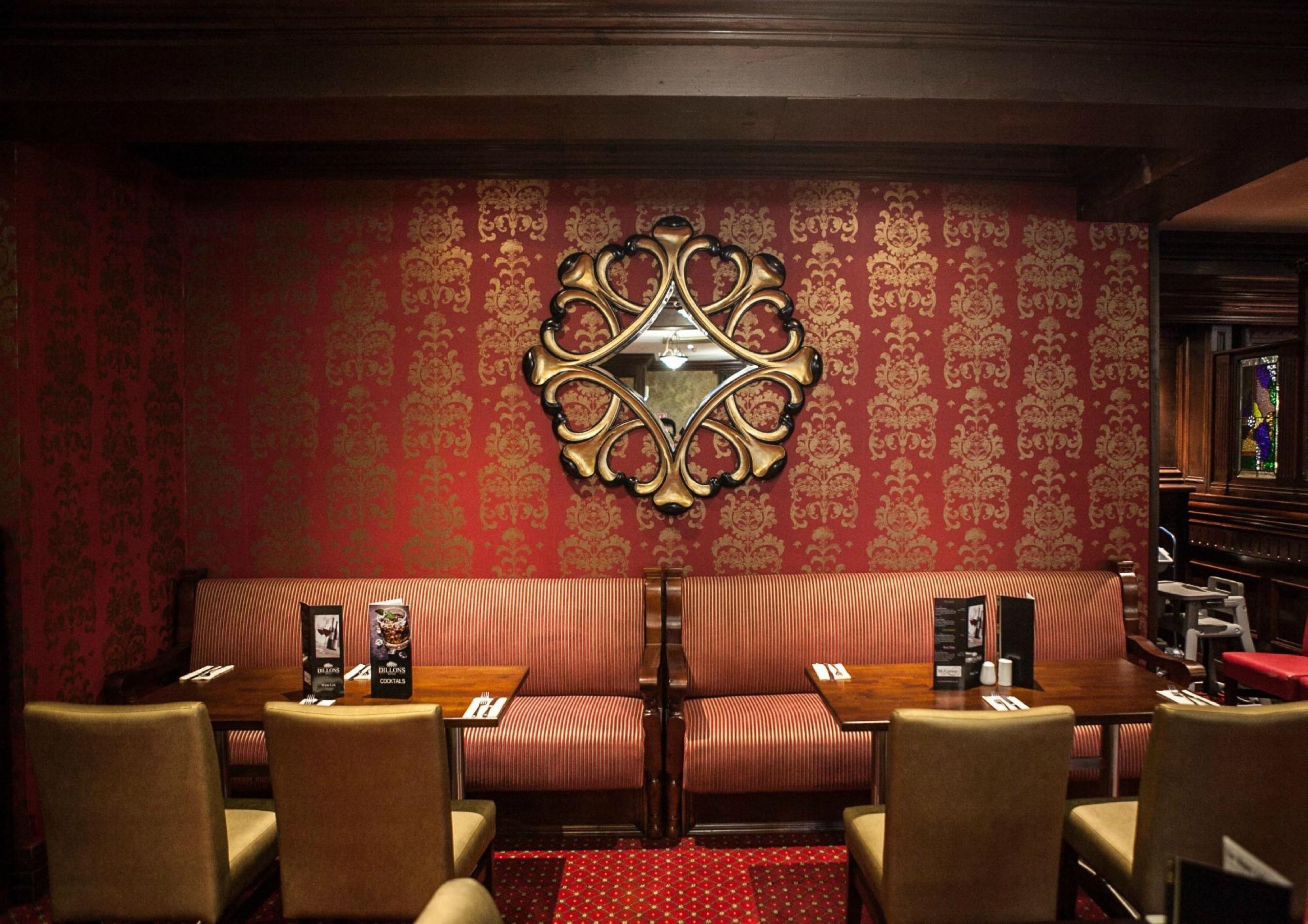 A restaurant with a red patterned wall, a decorative mirror, striped seating, and wooden tables.