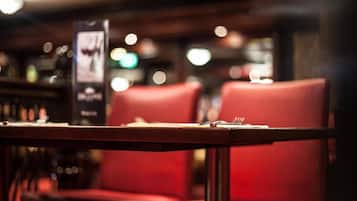 A restaurant interior with red upholstered chairs and a table set for two, featuring a menu stand.