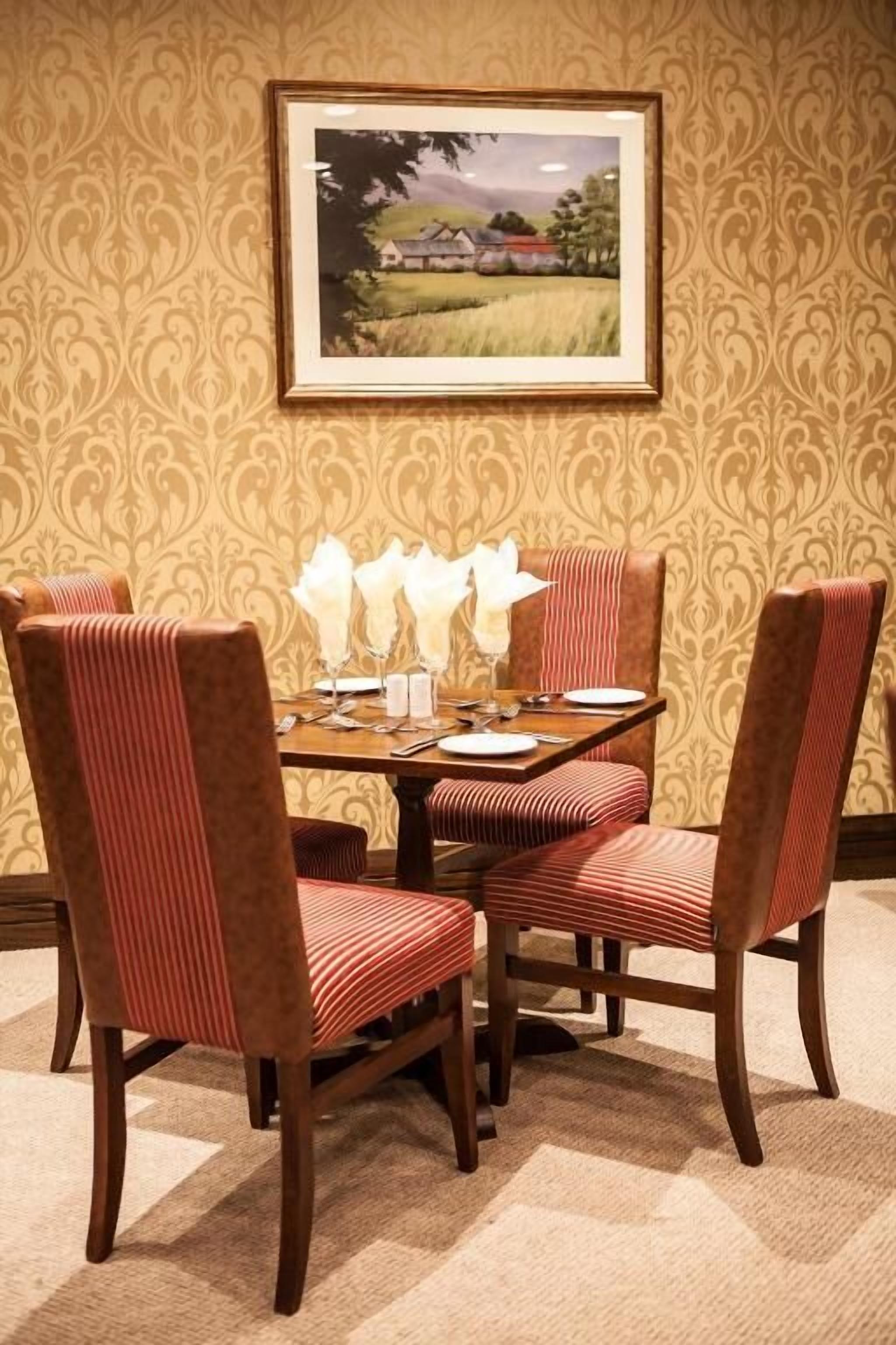 Un comedor con una mesa lista para cuatro personas, rodeada de sillas tapizadas con estampado a rayas.