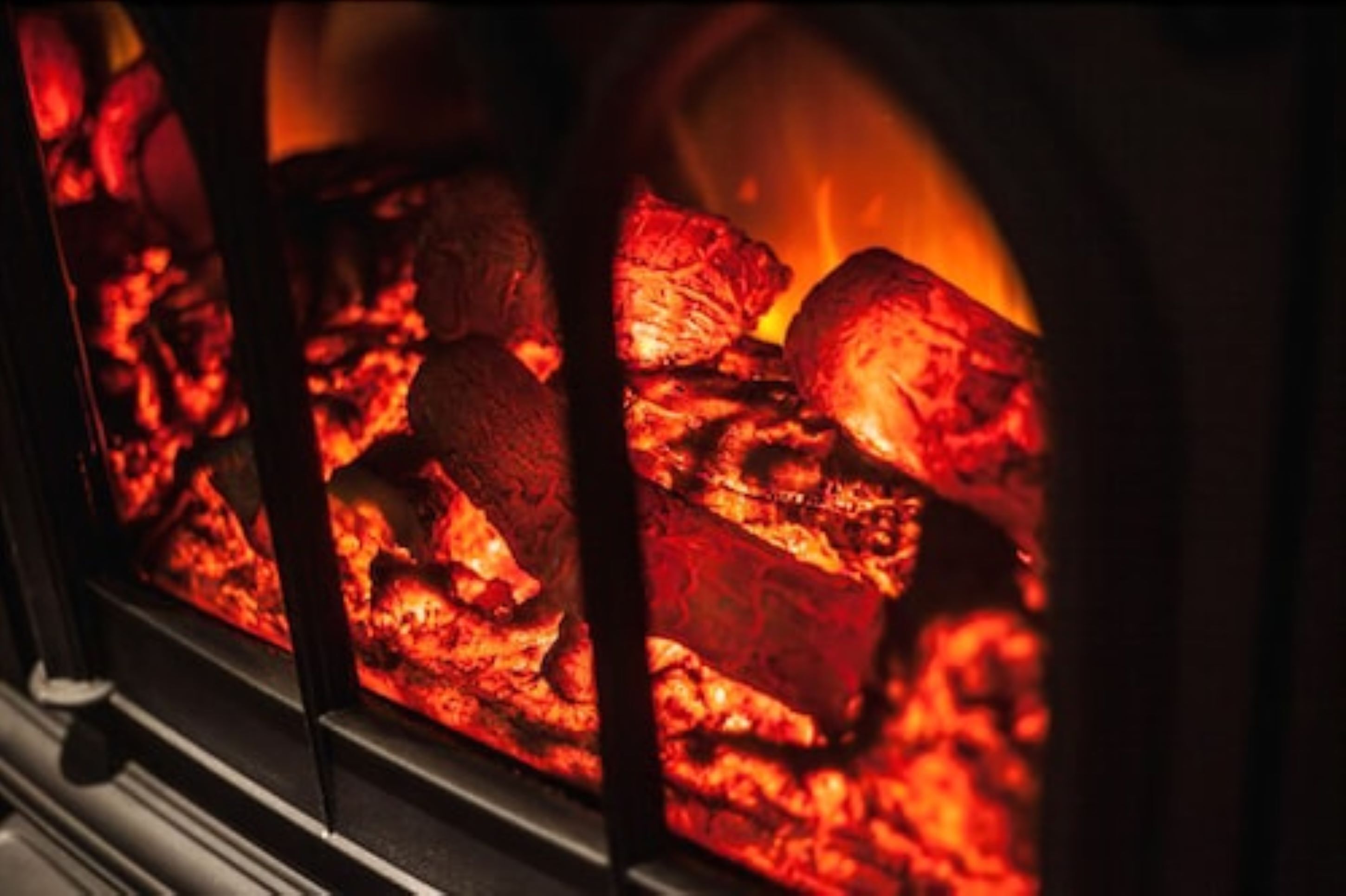 A close-up of a wood-burning stove with glowing embers and logs.