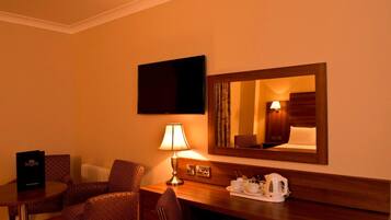 A hotel room with a TV, a desk with a lamp, a coffee maker, and a mirror.