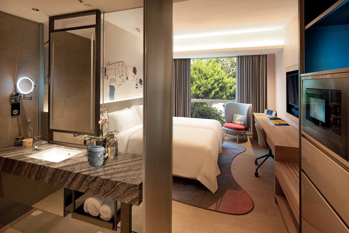 Une chambre d’hôtel moderne dotée d’un meuble-lavabo en marbre, d’un grand lit, d’un bureau avec un ordinateur et d’une télévision.