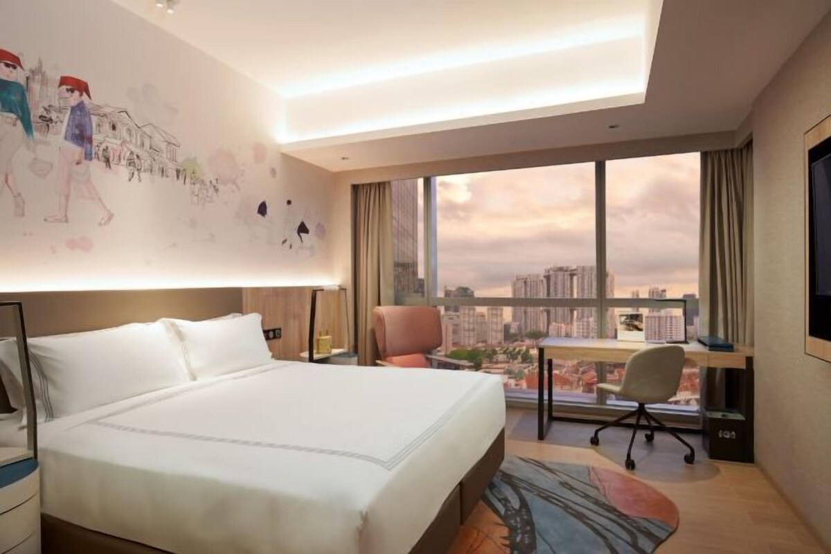 A hotel room with a large bed, a desk, and a view of the cityscape.