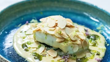 A dish with sliced almonds on top, served on a blue plate.