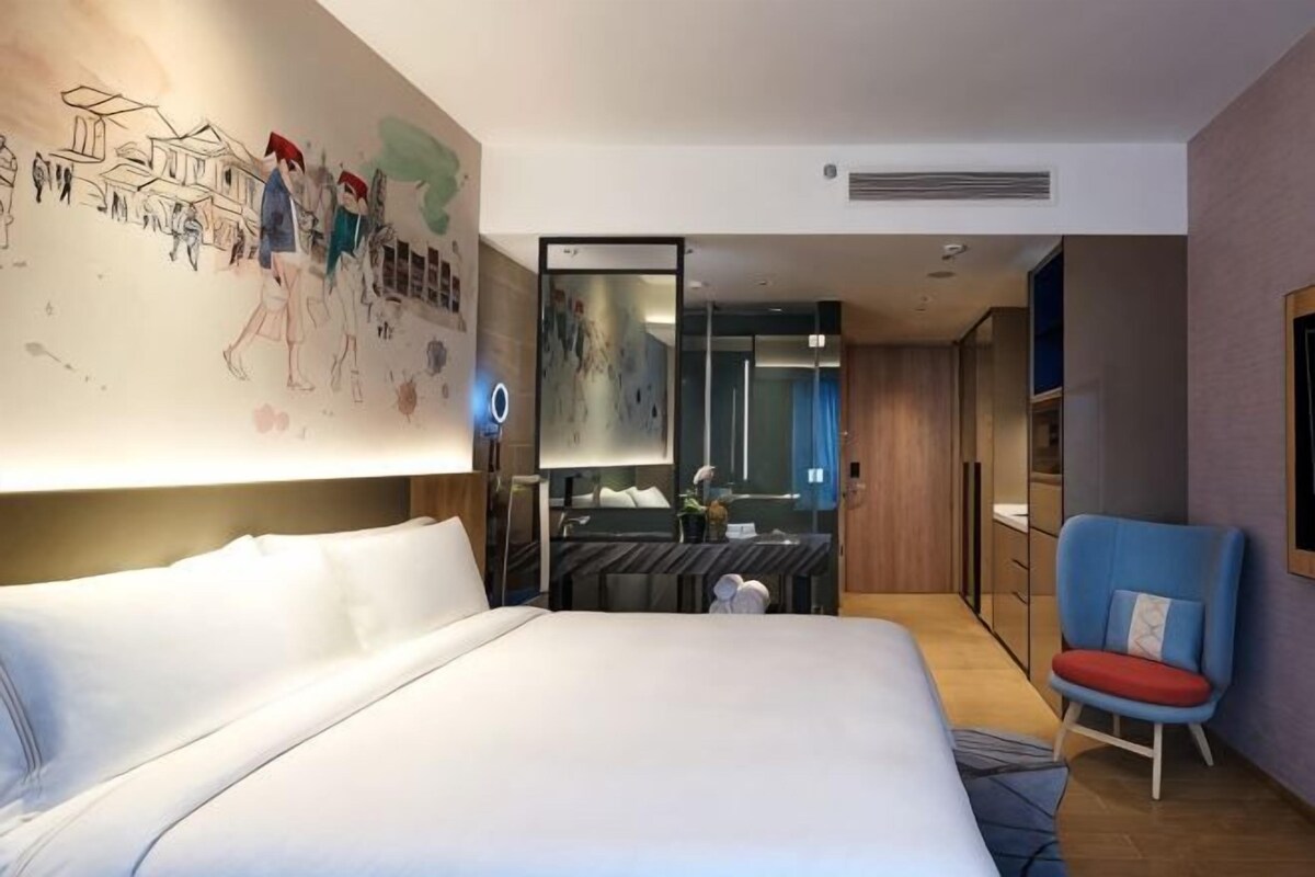A hotel room with a large bed, a desk with a chair, a mirror, and a wall with a mural.
