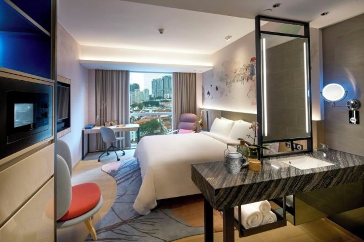 A hotel room with a bed, a desk, a chair, a TV, a bathroom with a mirror, and a view of the city.