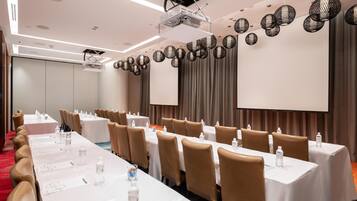 A conference room with long tables, chairs, and a projector screen.
